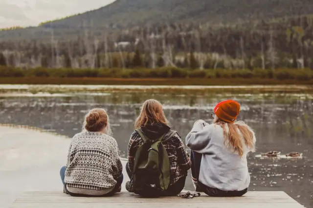 Three friends sitting side by side on a dock, looking at a lake