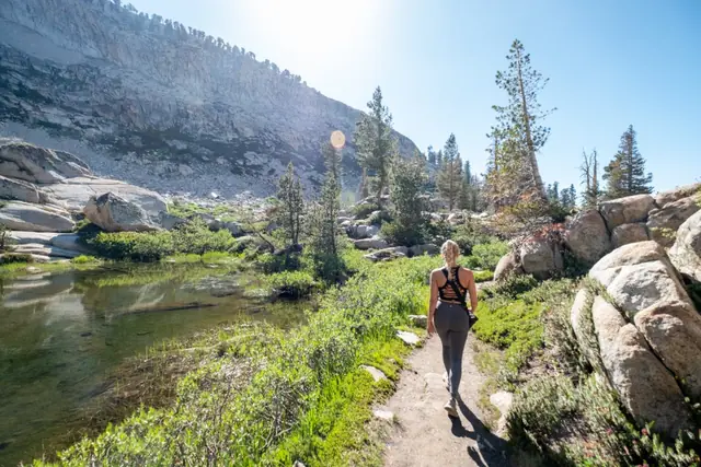 A woman walking on a trail between rocks and pine trees on a sunny day