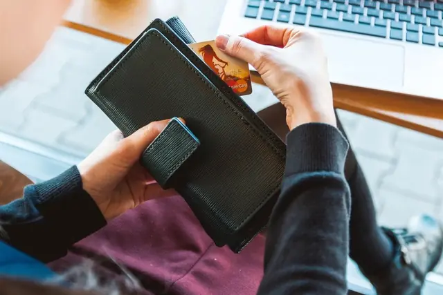 Hands taking a bank card out of a wallet in front of a laptop