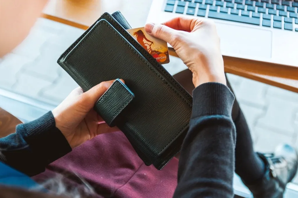 Hands taking a bank card out of a wallet in front of a laptop