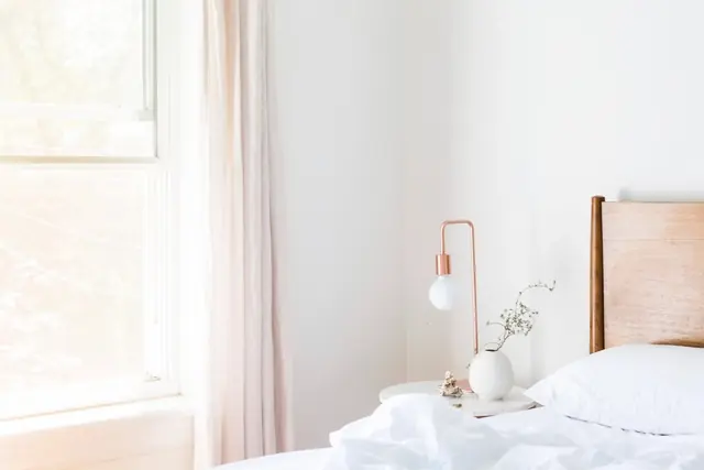 A bright bedroom with white bedding, a copper lamp and a window