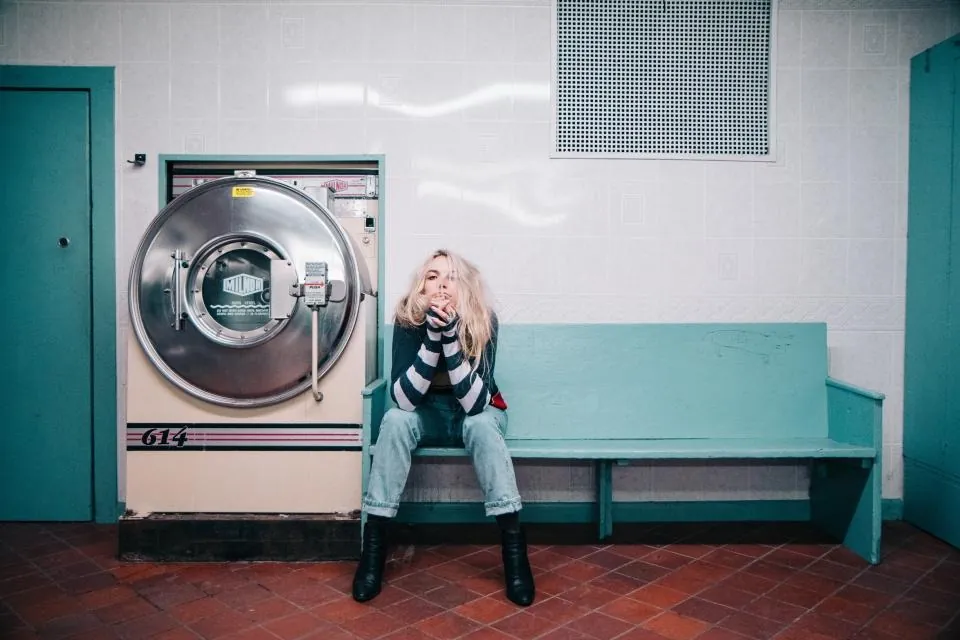 A woman sitting on a bench next to an industrial washing machine in a laundromat