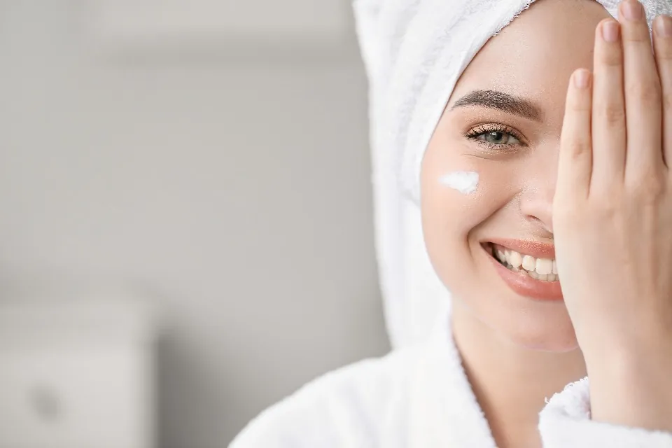 A smiling woman in a towel with a dab of cream on her cheek